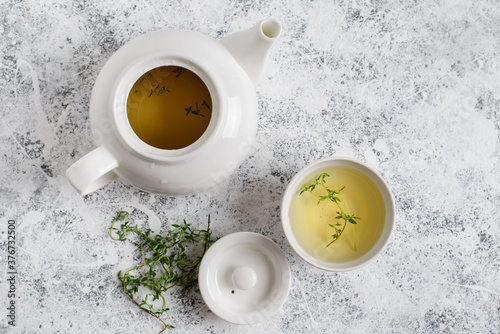 Herbal tea in white teapot and white boul and thyme stalks on light textured background, top view