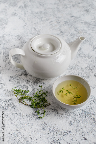 Herbal tea in white teapot and white boul and thyme stalks on light textured background