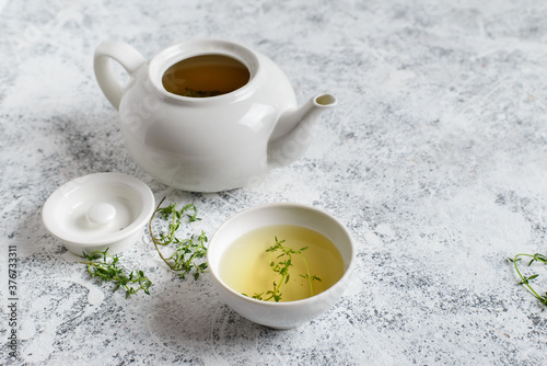 Herbal tea in white teapot and white boul and thyme stalks on light textured background