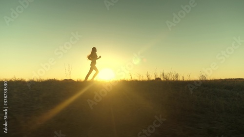 running after sun. training jogging. healthy beautiful girl is engaged in fitness, jogging in country in sun. Jogger girl breathes fresh air on field. Free young woman runs in summer park at sunset.