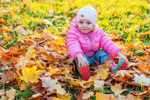 Happy young girl playing under falling yellow leaves in beautiful autumn park on nature walks outdoors. Little child throws up autumn orange maple leaves. Hello autumn concept.