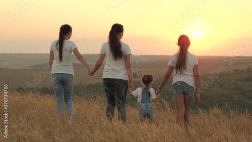 healthy family  mom and daughters are walking in field at sunset in mountains  children are holding mom s hands. happy children and parent walk in rays of the beautiful sun  travel. happy family