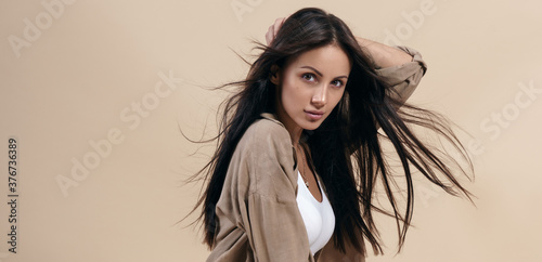 Portrait of pretty brunette girl with healthy long hair on beige background with copy space