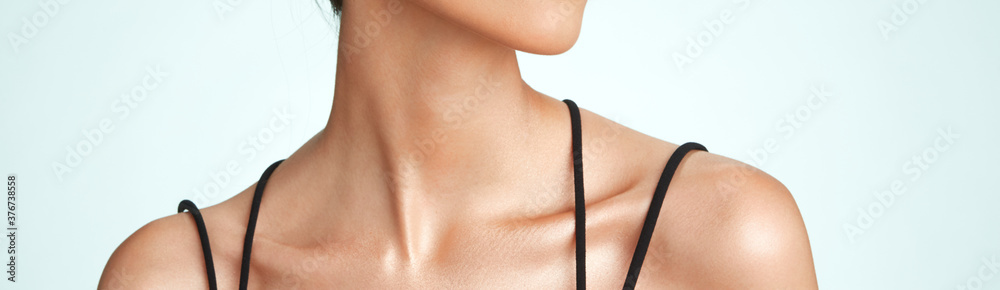 young mixed race women against a light blue background showing nape of her neck and collarbone modelling skin care and flawless skin wearing black strap shirt
