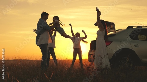 parents and children stopped for halt. dad, mom and daughters dance and admire beautiful sunset. happy family travels by car. Car travel. family, happy childhood.daddy throws happy daughter into sky
