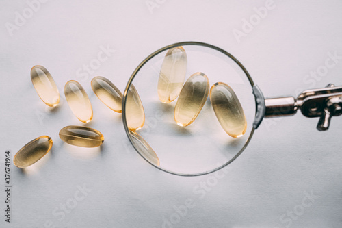 yellow transparent omega 3 capsules under a magnifying glass. food additive development concept