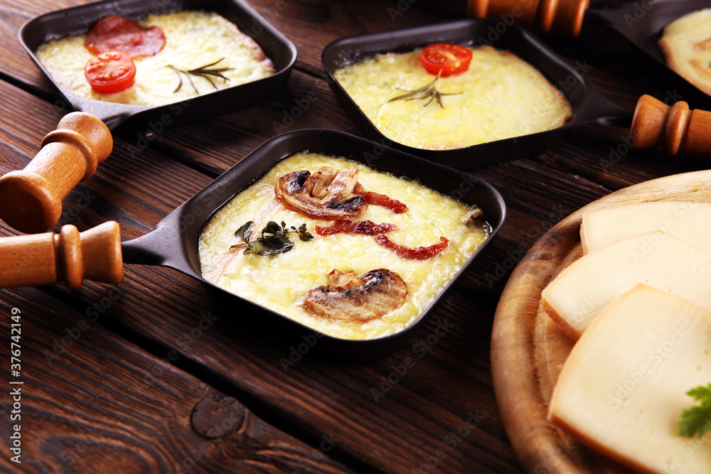 Delicious traditional Swiss melted raclette cheese served in individual skillets with salami and bacon