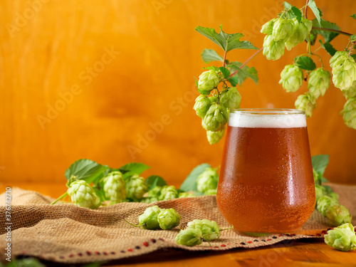 Photo A glass of hopped beer or IPA on a wooden table with hop cones