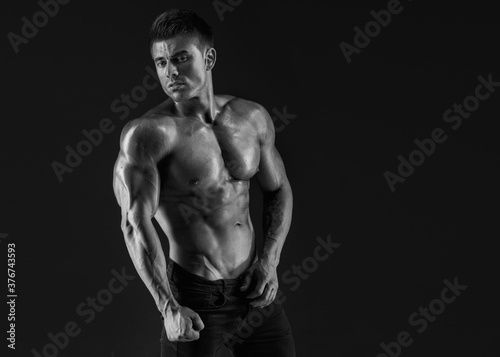 Muscular model sports young man on dark background. Fashion portrait of strong brutal guy. Sexy torso. Male flexing his muscles. © KDdesignphoto