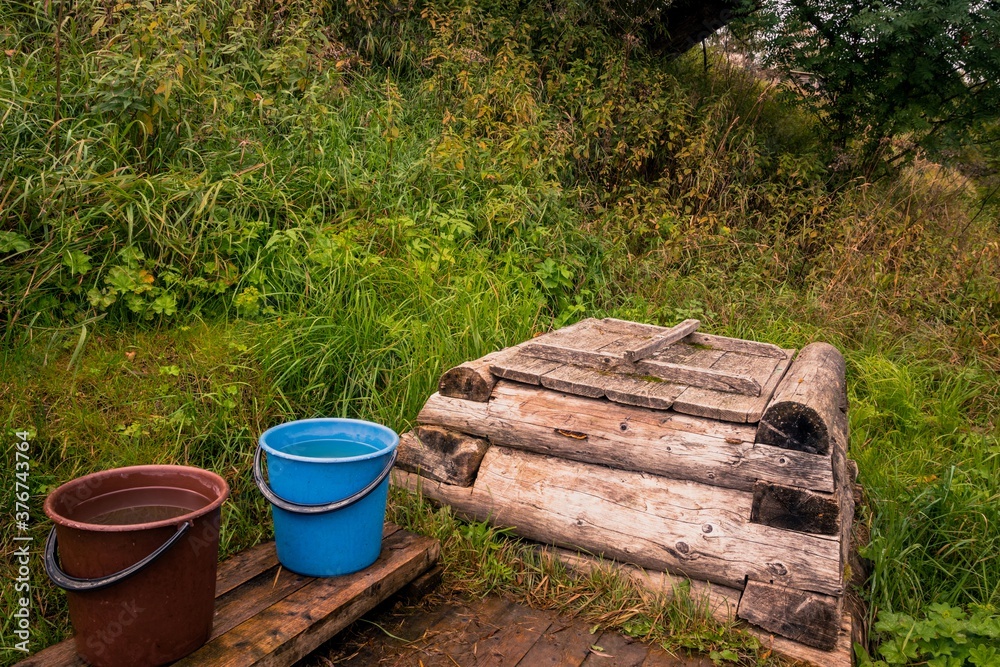 Rural retro landscape with wooden well and buckets of water on a hillside with green grass Rural retro landscape with wooden well and buckets of water on a hillside with green grass