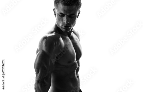 Muscular model sports young man on white background. Black and white fashion portrait of strong brutal guy. Sexy torso. Male flexing his muscles.