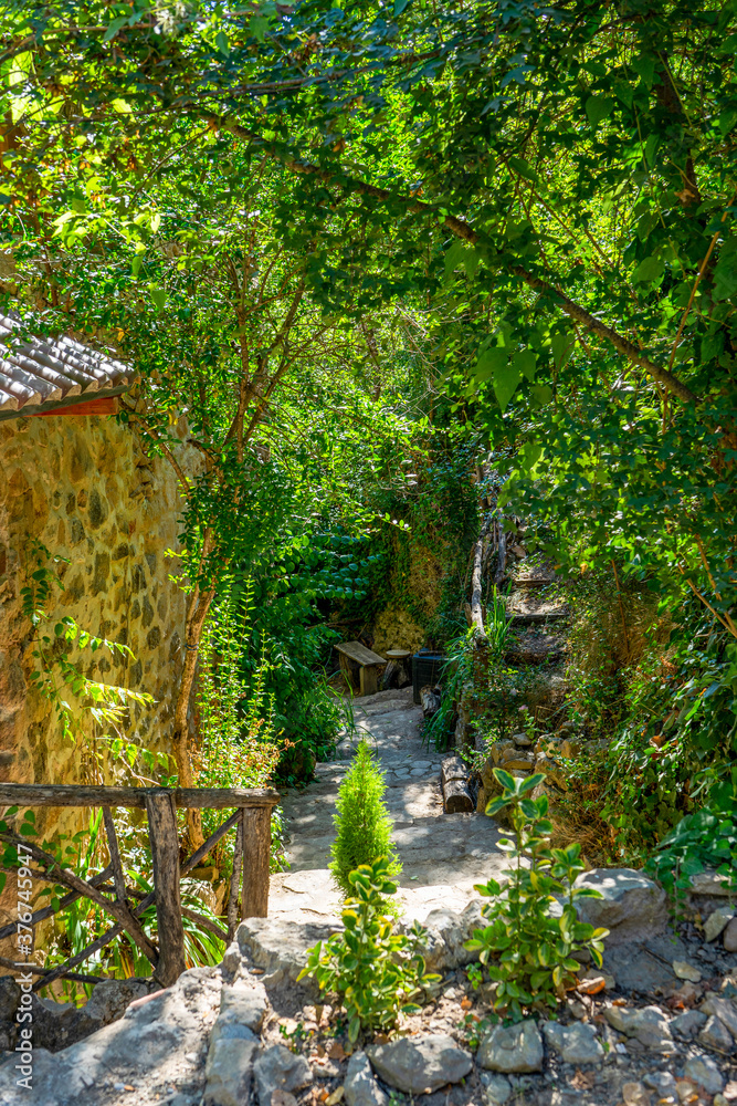 Nice driveway to an old stone house with fences and wooden stools and decorated with lots of greenery. Selective focus Nice driveway to an old stone house with fences and wooden stools and decorated with lots of greenery. Selective focus