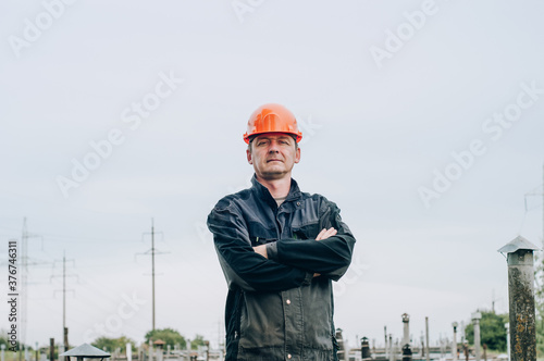 Young construction worker in overalls and orange safety helmet near construction metal coil store photo