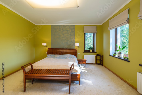 Modern interior of bedroom in apartment. Flowers on windowsills. Wooden bed and nightstand.