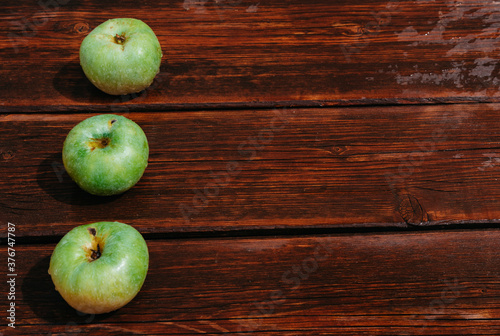 Fresh autumn Apple harvest on the kitchen countertop. Three fresh green apples lie in a row on a wooden table. A textured mahogany wood background and fruit lie on it.