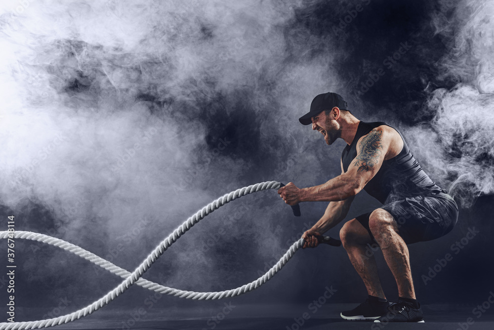 Bearded athletic looking bodybulder work out with battle rope on