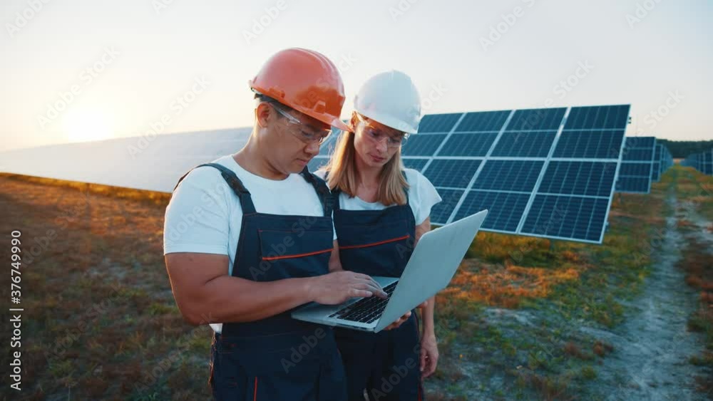 Professional male and female technicians exploring solar farm using laptop computer futuristic technologies in power plant landscape. Sustainable energy. Solar field. Professional male and female technicians exploring solar farm using laptop computer futuristic technologies in power plant landscape. Sustainable energy. Solar field.