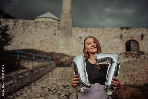 Woman with balloons and with number 17 balloons posing on his birthday, i background old town