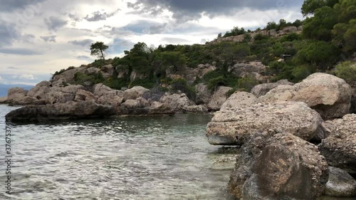 A grey cliff in a bay and trasparent sea in Spetses island in Greece in a cloudy day