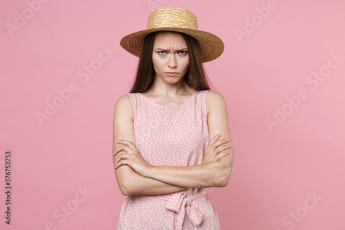 Fotografía Displeased offended dissatisfied young brunette woman 20s wearing pink summer dotted dress hat posing holding hands crossed looking camera isolated on pastel pink color background studio portrait