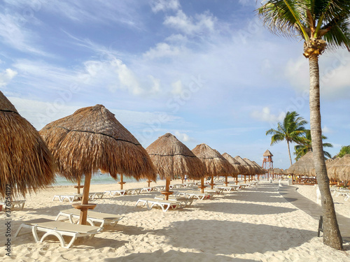 Detalle de un grupo de palapas y palmeras en una playa del caribe con un cielo azul como fondo.