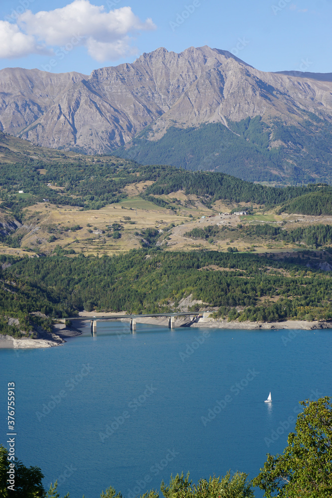 Fototapeta premium view of Serre Ponçon lake, France in the mountains with a lone sailboat