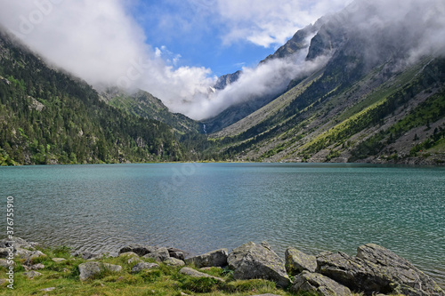 Green and cloudy mountain landscape with a large lake of transparent water, trees and clouds.