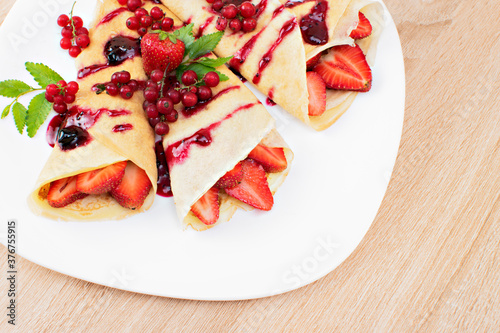 Pancakes with cranberries and strawberries on a plate. Pancakes with berries, strawberries and chocolate syrup. Breakfast with pancakes with strawberries and berries on a plate..