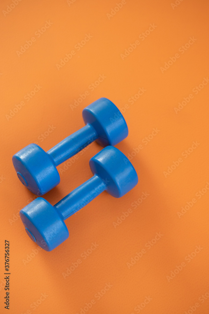 a pair of blue dumbbells on orange background. copy space. a pair of blue dumbbells on orange background. copy space.