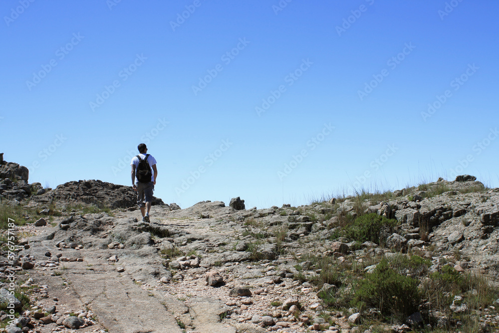 Fototapeta premium Outdoor activities. Hiking. View of a young adult hiker, walking along the dirt path in the rocky mountain top. 