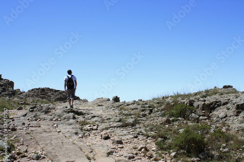 Outdoor activities. Hiking. View of a young adult hiker, walking along the dirt path in the rocky mountain top. 