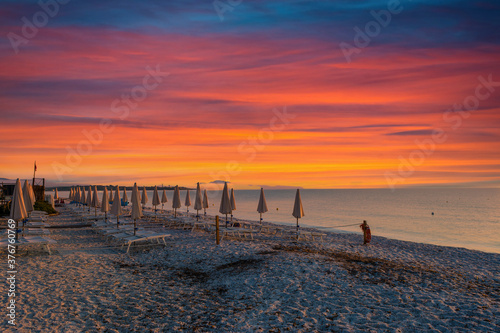 rows of closed umbrellas on the beach at dramatic colorful sunrise