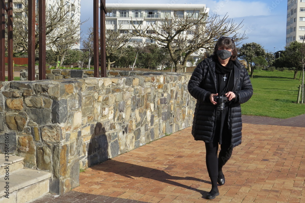 Woman walking in the park with a facemask on and a camera in hand