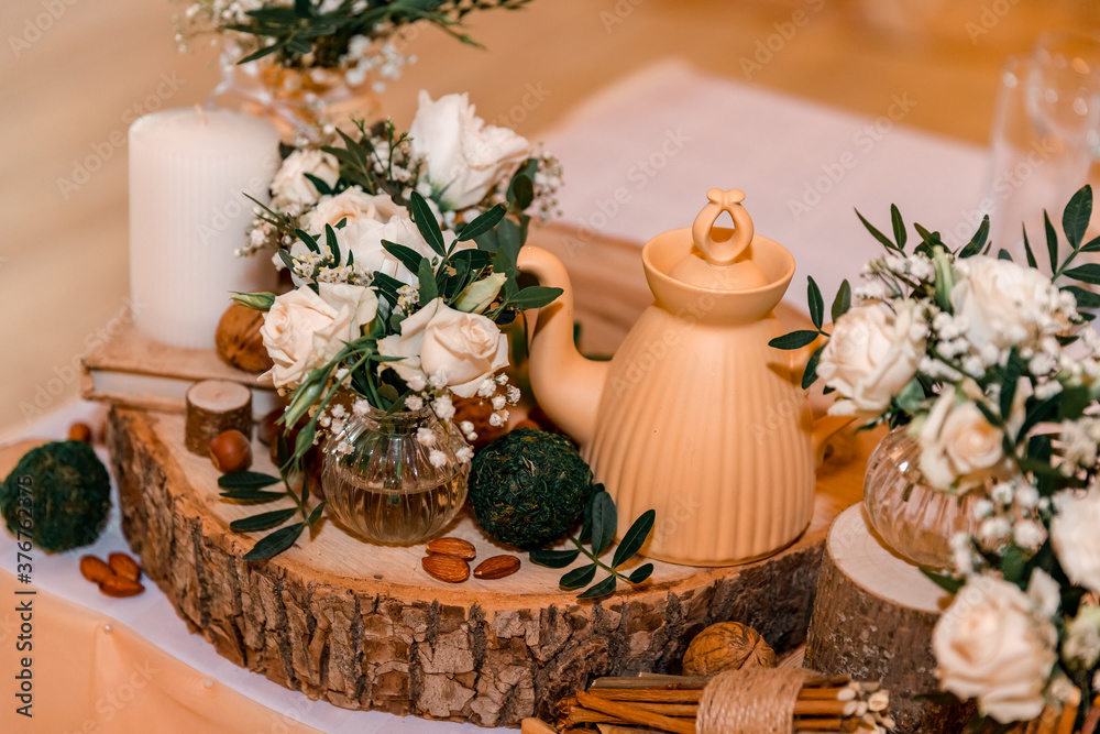 Wedding decor in rustic style. Wedding table decoration with sawed wood, white roses and green leavers in a bouquet, glass vases , teapot and nuts. Wedding decor in rustic style. Wedding table decoration with sawed wood, white roses and green leavers in a bouquet, glass vases , teapot and nuts.