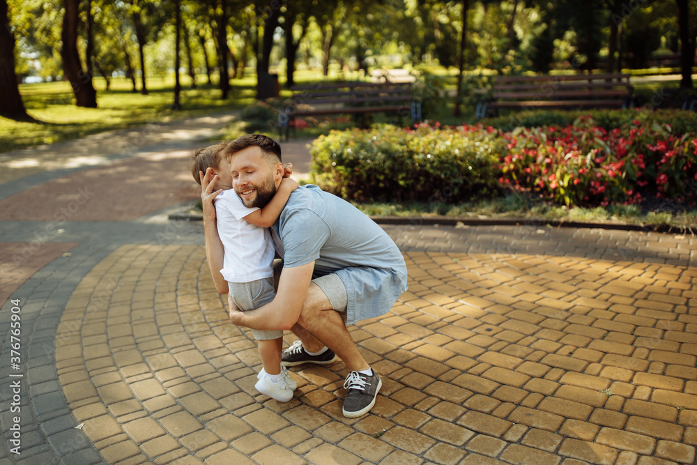 Fototapeta premium Overjoyed man with little boy at the park, lovely son hugging caring father, smiling, dad and toddler spend time together, enjoy tender family moments, parenthood concept