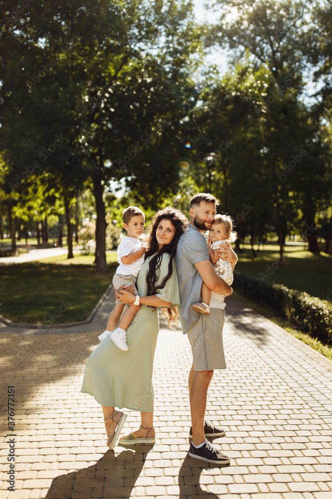 Obraz premium Overjoyed family with little kids at the park, caring dad hold in arms adorable daughter, joyful son sitting on mother hands, smiling, enjoy parenting, childhood concept