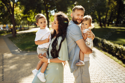 Adorable parents with little children walking at the park, caring mother hold in arms happy son, cute daughter sitting on father hands, smiling, parenthood and childhood concept © shunevich