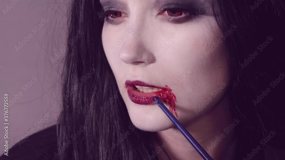 Young woman doing halloween makeup with blod from mouth