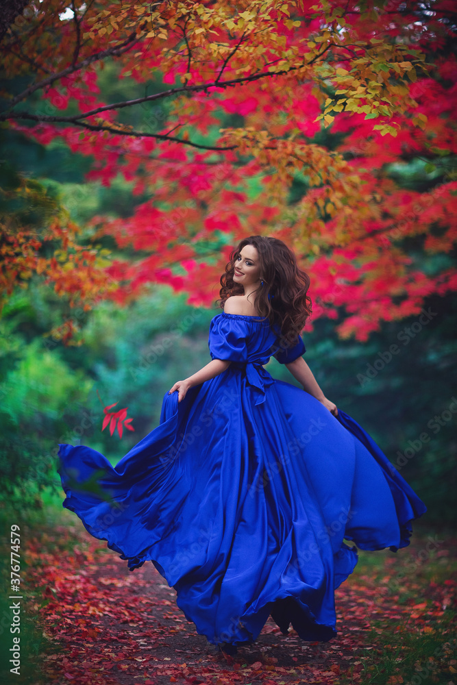 Romantic portrait of a beautiful young girl in a long ultramarine blue dress running away on the background of an autumn рark with red leaves Romantic portrait of a beautiful young girl in a long ultramarine blue dress running away on the background of an autumn рark with red leaves