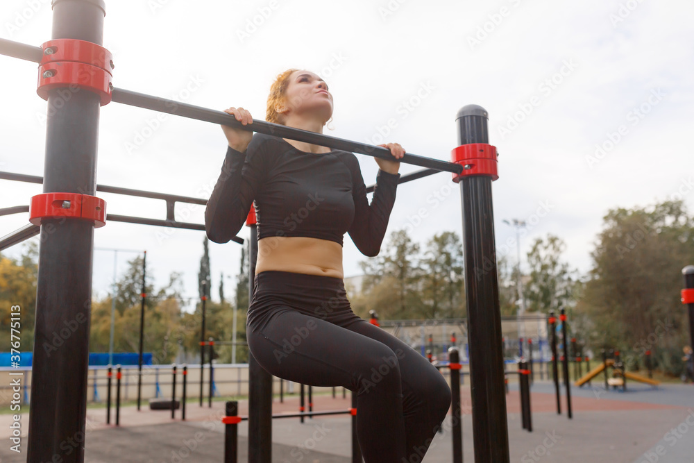 young attractive woman performs pull-ups on the horizontal bar on the workout site
