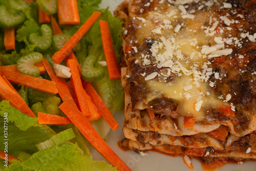 closeup de porcion de lasaña boloñesa con ensalada de zanahoria lechiga y apio