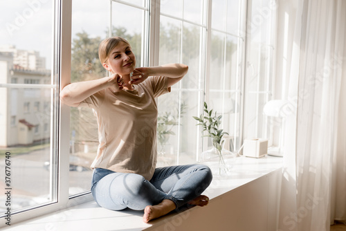 Free Download Smiling pretty woman sitting on a windowsill at home at the early morning - GFXLoad