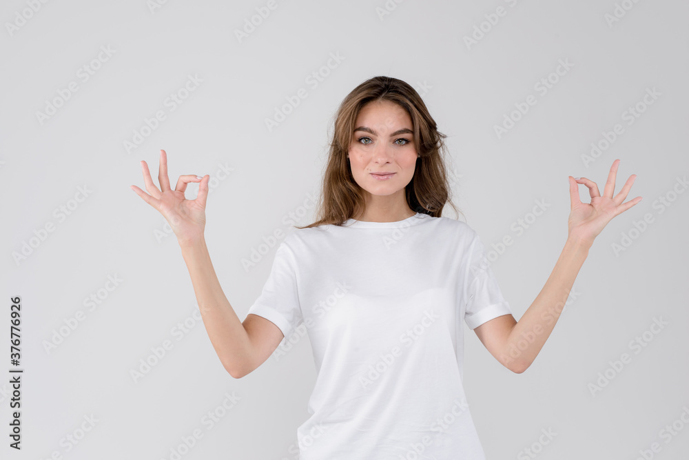 Young smiling woman showing okey gesture sign looking at camera, isolated on white grey studio background Young smiling woman showing okey gesture sign looking at camera, isolated on white grey studio background
