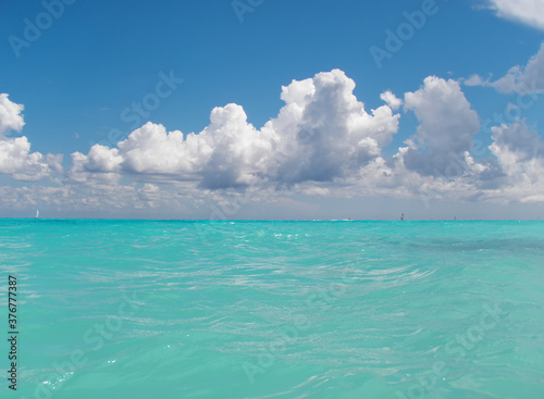 Fototapeta Naklejka Na Ścianę i Meble -  View over the surface of the water of the Caribbean Sea, in the background sailing boats, the blue sky, and white clouds. Playa del Carmen, Mexico
