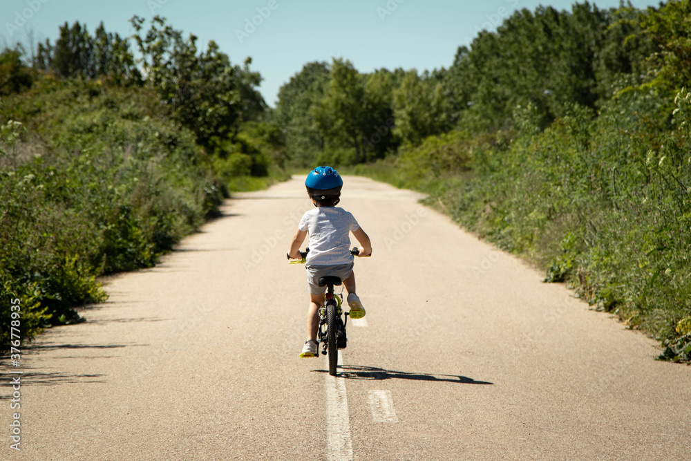 Fototapeta premium Niño pedaleando en su bici por una carretera rodeada de mucha vegetación