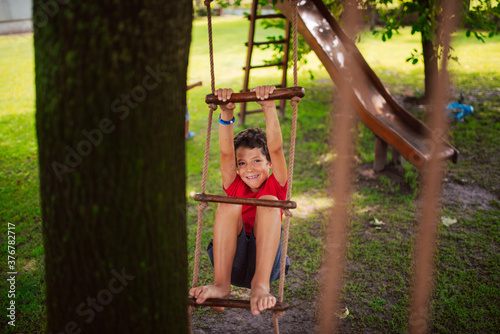 A beautiful little caucasian boy on a wooden ladder for children in the park. A day in nature