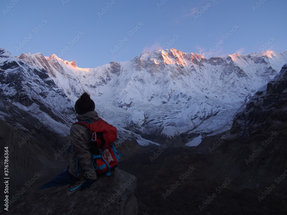Fototapeta premium A climber sits on a rock and watches the sunrise over a snow-covered rock, ABC (Annapurna Base Camp) Trek, Annapurna, Nepal