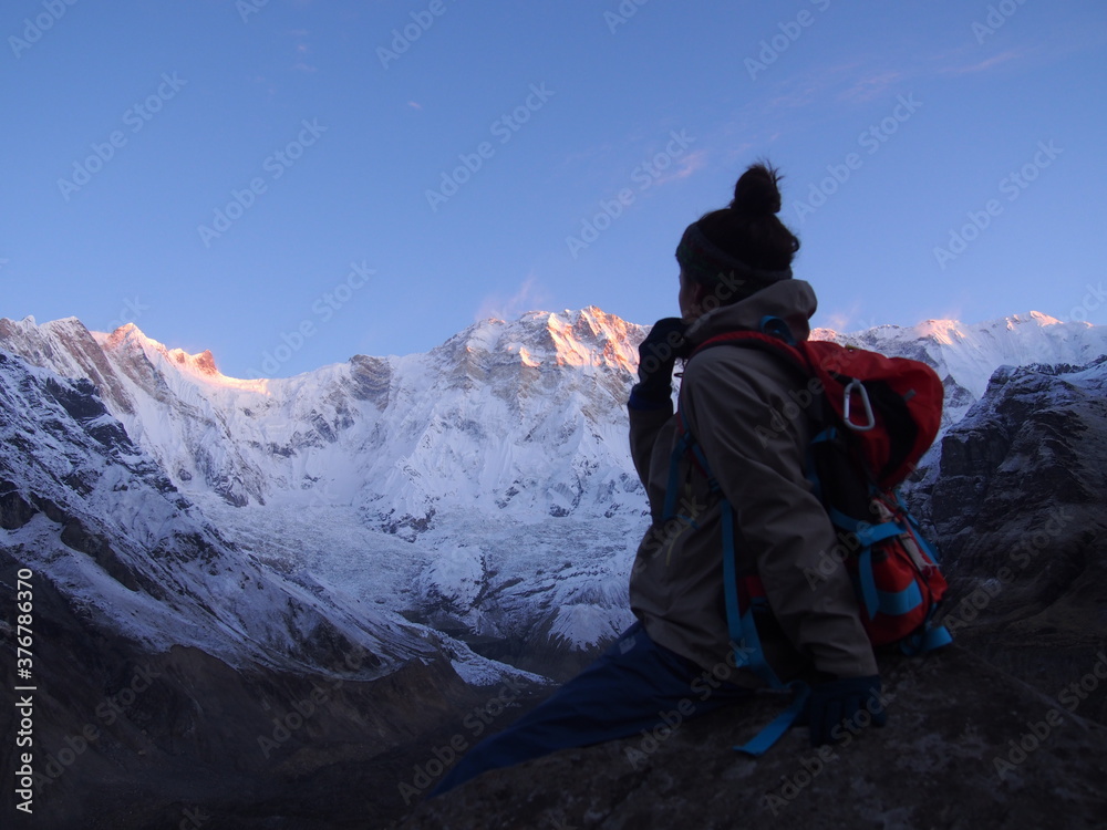 A climber sits on a rock and watches the sunrise over a snow-covered rock, ABC (Annapurna Base Camp) Trek, Annapurna, Nepal
