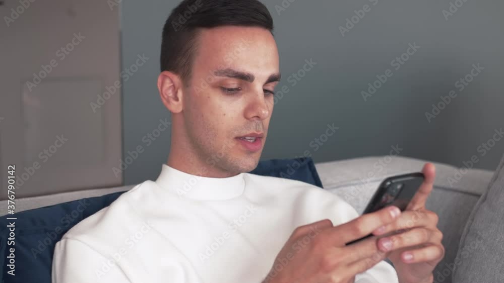 Young caucasian guy using phone relax on sofa at home Young caucasian guy using phone relax on sofa at home