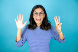 Pretty woman wearing glasses standing over insolated blue background showing and pointing up with fingers number eight while smiling confident and happy